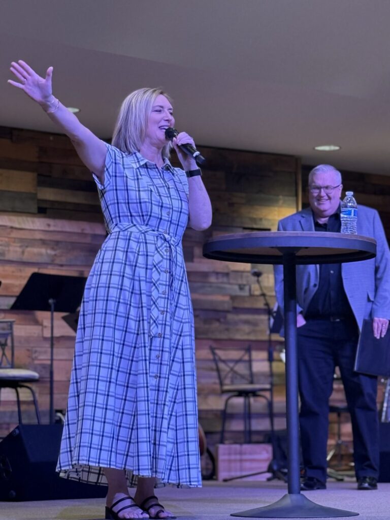 A pretty woman giving a speech to a live audience, speaking confidently and smiling